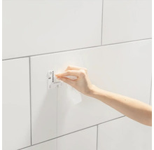 Eine Person befestigt eine Grohe Abdeckplatte auf einer gefliesten Wand.