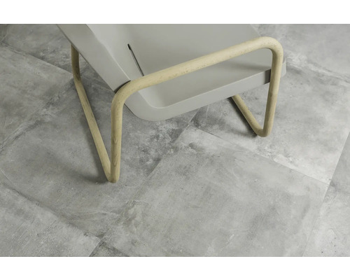 Detailansicht eines grauen Stuhls mit Holzbeinen auf grauem Fliesenboden