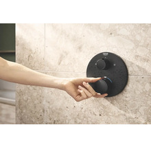 Eine Hand bedient einen Grohe Duschthermostat an einer gefliesten Wand