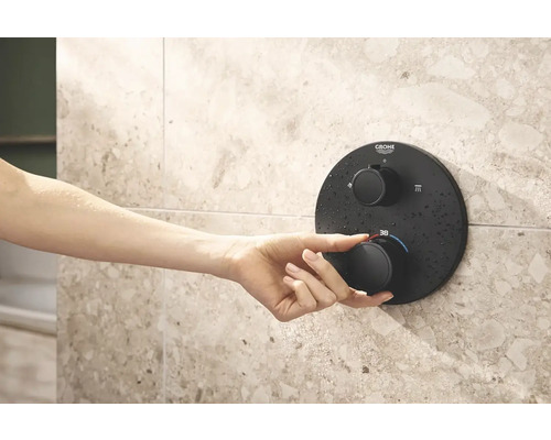 Eine Hand bedient einen Grohe Duschthermostat an einer gefliesten Wand