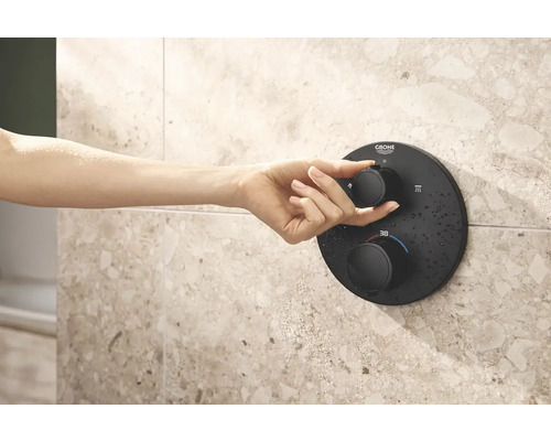 Hand bedient schwarzen Duschthermostat von Grohe an gefliester Wand