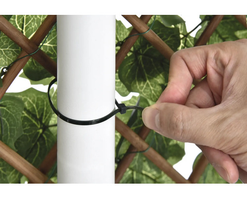 Eine Person befestigt einen Sichtschutzzaun mit einem Kabelbinder an einem Pfosten.