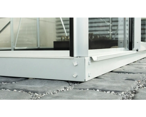 Detailaufnahme der Basis eines Gewächshauses auf Steinpflaster.