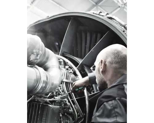 Ein Mann inspiziert und wartet ein Triebwerk mit einem Schraubendreher.