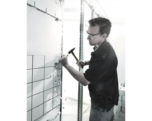 Handwerker mit Schutzbrille entfernt Fliesen mit Hammer und Meißel von einer Wand.