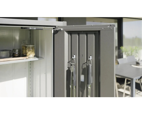 Geöffneter Metall Gartenschrank mit Regalböden und Grillwerkzeugen an der Innenseite der Tür