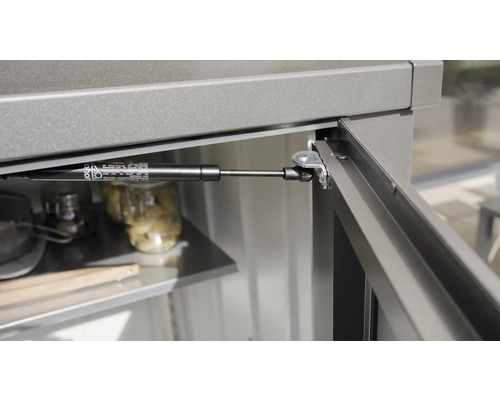 Detailansicht einer Gasdruckfeder an einem grauen Schrank