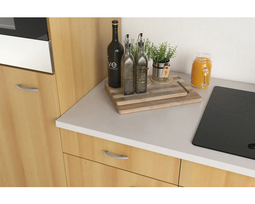 Küchenszene mit Schneidebrett, Ölflaschen, Kräutern und Kochfeld auf einer Küchentheke.