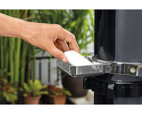 Eine Hand legt ein Stück Seife in eine Seifenschale an einem Wasserhahn im Garten