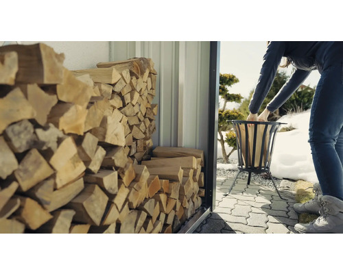 Frau befüllt Feuerkorb mit Holz aus einem Holzregal