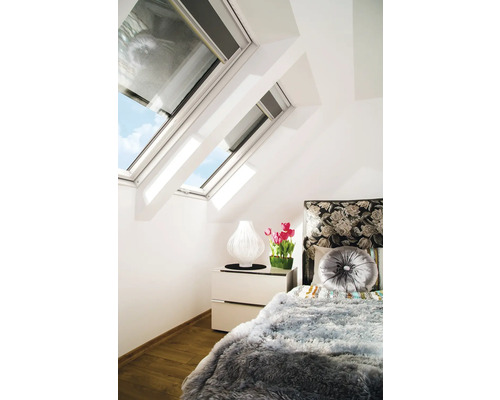 Schlafzimmer mit Dachfenstern, Nachttischlampe, Tulpen und einem Bett mit Kissen