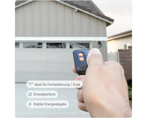 Garagentoröffner-Fernbedienung in der Hand vor Garage