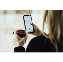 Frau mit Tasse und Smartphone zur Temperaturregelung