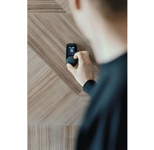 Person, die einen Smart Home Thermostat an einer Holzwand einstellt