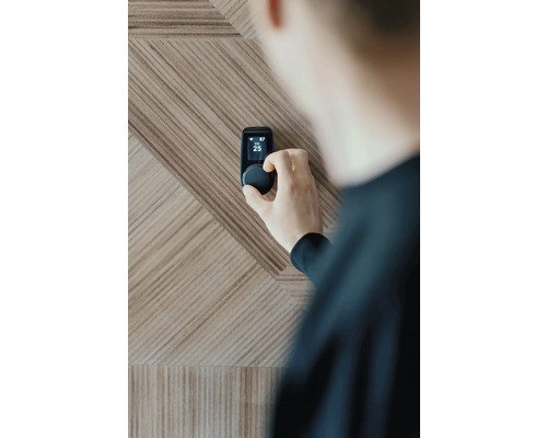 Person, die einen Smart Home Thermostat an einer Holzwand einstellt