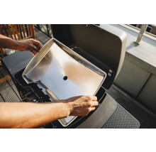 Person setzt eine Fettauffangschale in einen Grill ein.