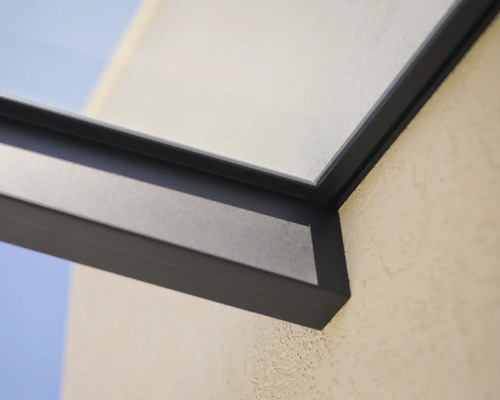 Detail eines dunklen Aluminiumrahmens für eine Terrassenüberdachung mit Glaselement an einer Außenwand.