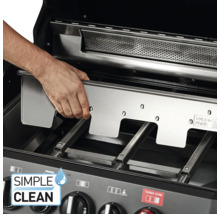 Eine Hand setzt eine Edelstahlplatte in einen Grill ein.