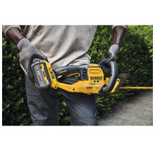 Eine Person hält eine gelbe DeWalt Akku-Heckenschere mit Akku in den Händen.