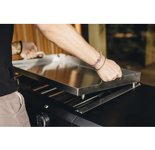 Eine Person befestigt eine Grillplatte auf einem Grill.