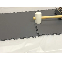 Verlegung von grauen, verzahnten Bodenfliesen mit Gummihammer