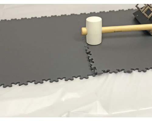 Verlegung von grauen, verzahnten Bodenfliesen mit Gummihammer