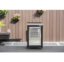 Mobiler Tenneker Outdoor-Kühlschrank mit Glastür und Rollen auf einer Terrasse vor einer Holzwand.