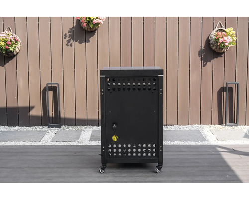 Mobiler Außenküchen-Unterschrank in Schwarz mit Lüftungsschlitzen und Stromanschluss auf einer Terrasse vor einem Holzzaun.