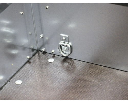 Zurröse aus Metall an einer Anhängerseitenwand zur Ladungssicherung über einem strukturierten Boden.
