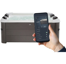 Hand hält Smartphone mit App zur Steuerung eines rechteckigen Whirlpools in grauer Holzoptik, zeigt Einstellungen wie 38 Grad und Massagefunktion.