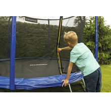 Ein Kind öffnet den gelben Reißverschluss am Sicherheitsnetz eines Marimex Trampolins mit blauer Randabdeckung im Garten.