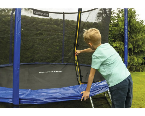 Ein Kind öffnet den gelben Reißverschluss am Sicherheitsnetz eines Marimex Trampolins mit blauer Randabdeckung im Garten.