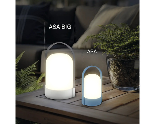 Zwei moderne LED-Laternen ASA BIG und ASA auf einem Holztisch, stimmungsvolle Außenbeleuchtung mit Pflanzen und Sofa im Hintergrund.