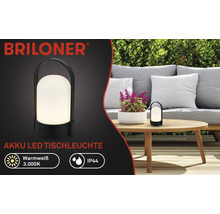 Briloner Logo, schwarze Akku LED Tischleuchte auf einem Holztisch im Garten, warmweißes Licht 3.000 Kelvin, Schutzart IP44.