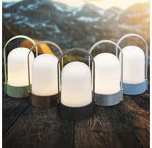 Fünf tragbare Outdoor-LED-Laternen in verschiedenen Farben auf einem Holztisch bei Regen vor einer Gebirgskulisse.