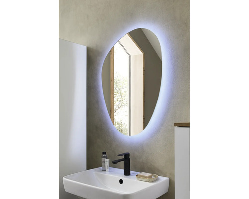 Asymmetrischer LED-Badspiegel über einem weißen Waschbecken mit schwarzer Armatur in einem modern gestalteten Badezimmer.