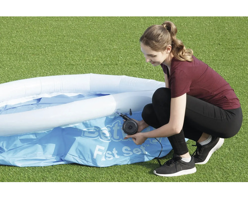 Eine Frau pumpt den oberen Ring eines aufblasbaren Bestway Fast Set Pools mit einer elektrischen Luftpumpe auf einer Rasenfläche auf.