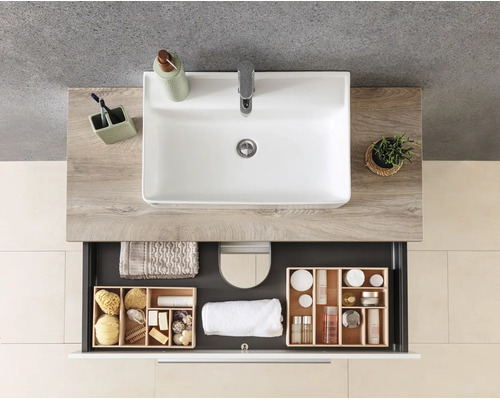 Moderner Waschtisch mit weißem Waschbecken auf Waschtischplatte in Holzoptik und offener Schublade mit Inneneinteilung aus Holz und Handtüchern.