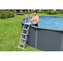 Graue Poolleiter an einem Aufstellpool mit Verkleidung in Holzoptik im Garten, mit einem Mann im Wasser.