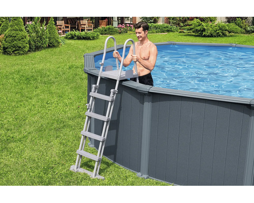 Graue Poolleiter an einem Aufstellpool mit Verkleidung in Holzoptik im Garten, mit einem Mann im Wasser.