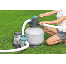 Sandfilteranlage für Pools mit Pumpe und Schläuchen, bedient von einer Person auf einer Rasenfläche.