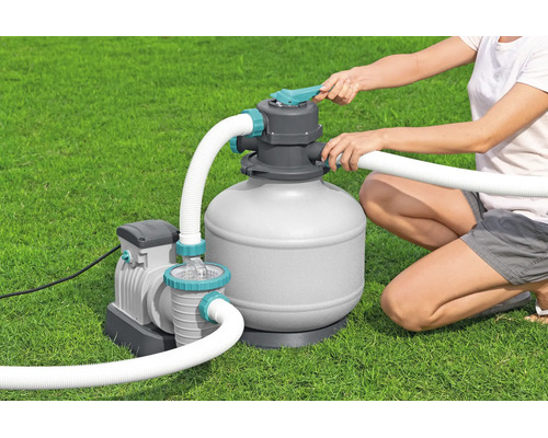 Sandfilteranlage für Pools mit Pumpe und Schläuchen, bedient von einer Person auf einer Rasenfläche.