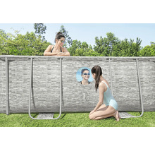 Aufstellpool mit Steinoptik-Außenwand und Sichtfenster im Garten, eine Frau im Pool und ein Mädchen schaut von außen durch das Fenster.