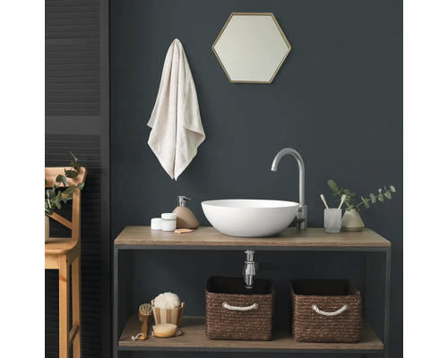 Modernes Badezimmer mit weißem Aufsatzwaschbecken auf einem Holzunterschrank, hoher silberner Armatur und hexagonalem Spiegel vor dunkler Wand.