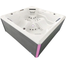 Quadratischer Außenwhirlpool mit grauer Verkleidung in Holzoptik, weißem Innenbecken, Massagedüsen und LED-Beleuchtung.