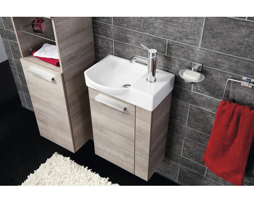 Modernes Badezimmer mit Waschbeckenunterschrank und Hochschrank in Holzoptik, Keramikwaschbecken und dunkler Fliesenwand.