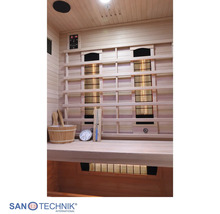 Innenansicht einer Infrarotkabine aus Holz mit Infrarotstrahlern, Steuerung, Saunakübel, Kelle, Sanduhr und Thermometer.