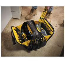 Offene Werkzeugtasche mit verschiedenen Hand- und Elektrowerkzeugen in mehreren Fächern auf einer Baustelle.