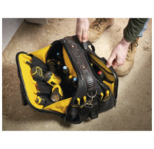 Person öffnet eine robuste Werkzeugtasche mit vielen Fächern, gefüllt mit Bohrschrauber, Taschenlampe und Schraubendrehern auf einer Baustelle.