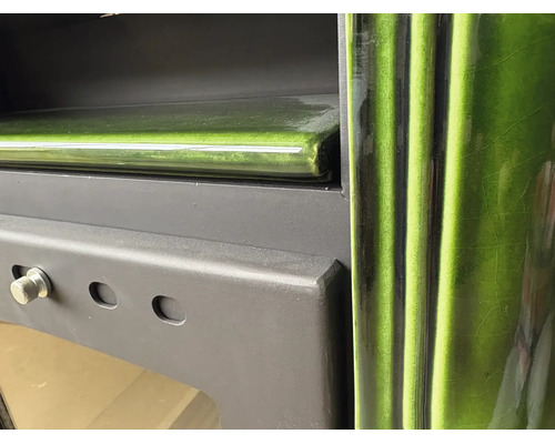 Detailansicht eines Kaminofens mit grüner Keramikverkleidung und mattschwarzem Metallgehäuse